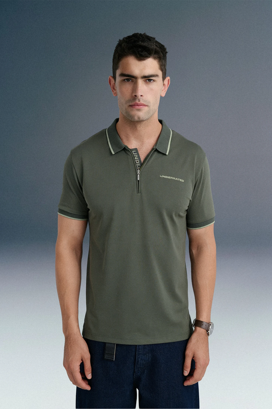 Front view from the waist up of a man looking forward, wearing a dark olive green polo shirt with subtle chest branding, paired with dark blue jeans.