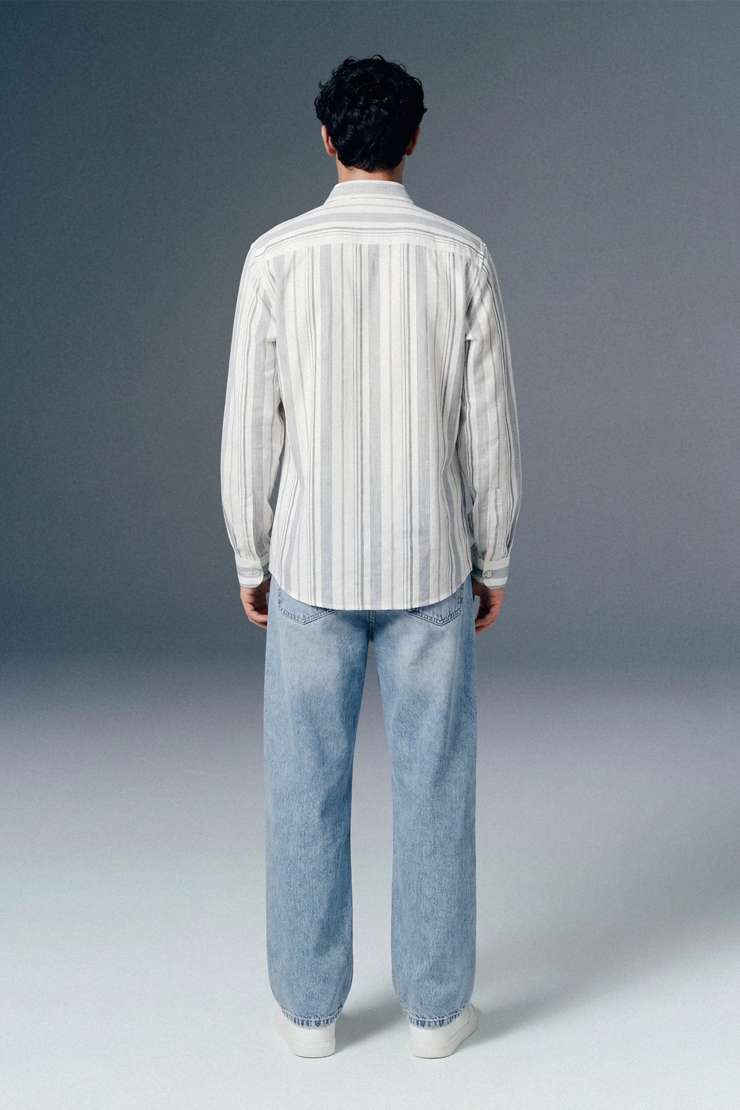 Person wearing a striped shirt and jeans from behind on a gray background