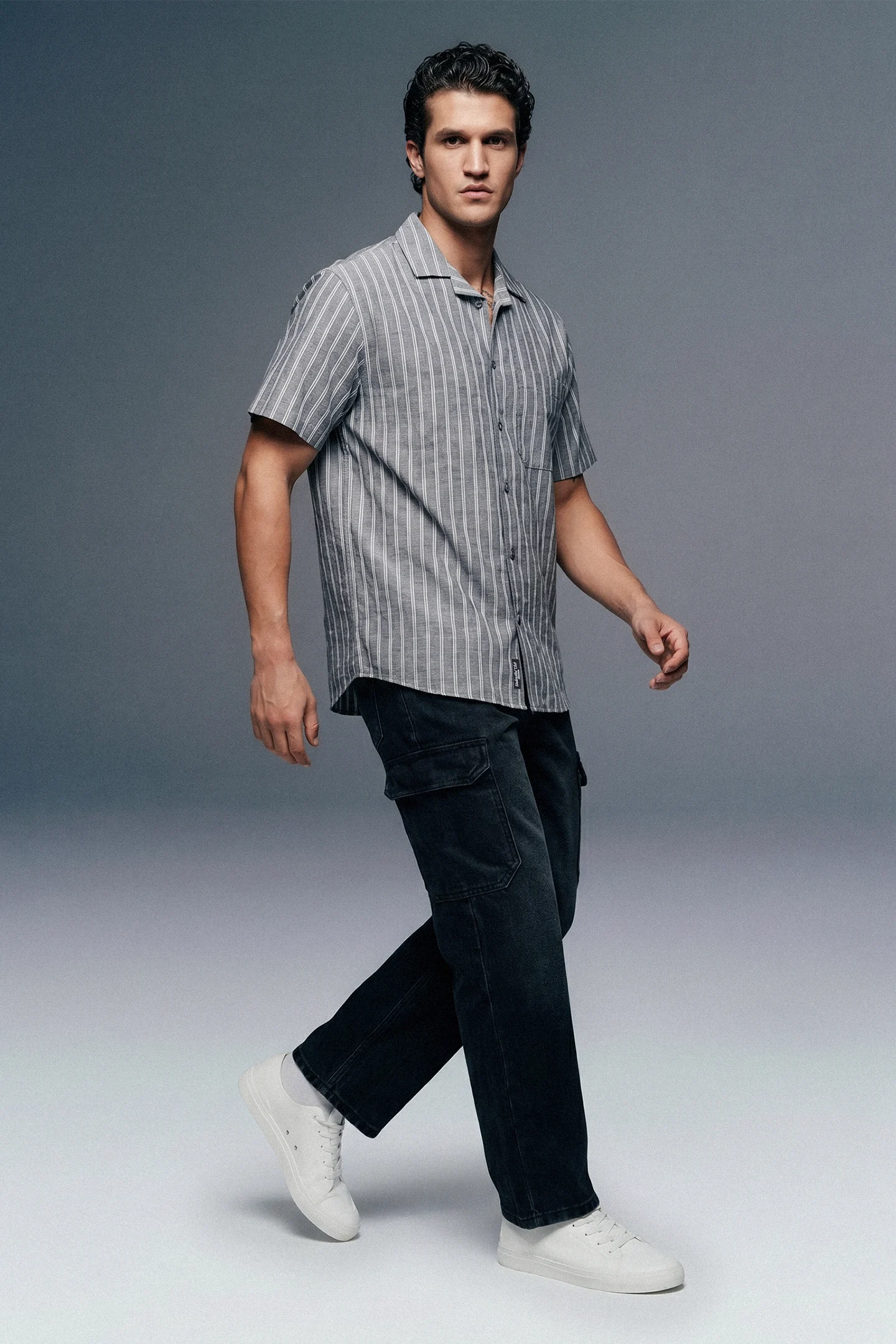 Man wearing a striped shirt and dark pants on a gray background