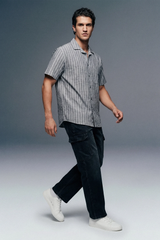 Man wearing a striped shirt and dark pants on a gray background