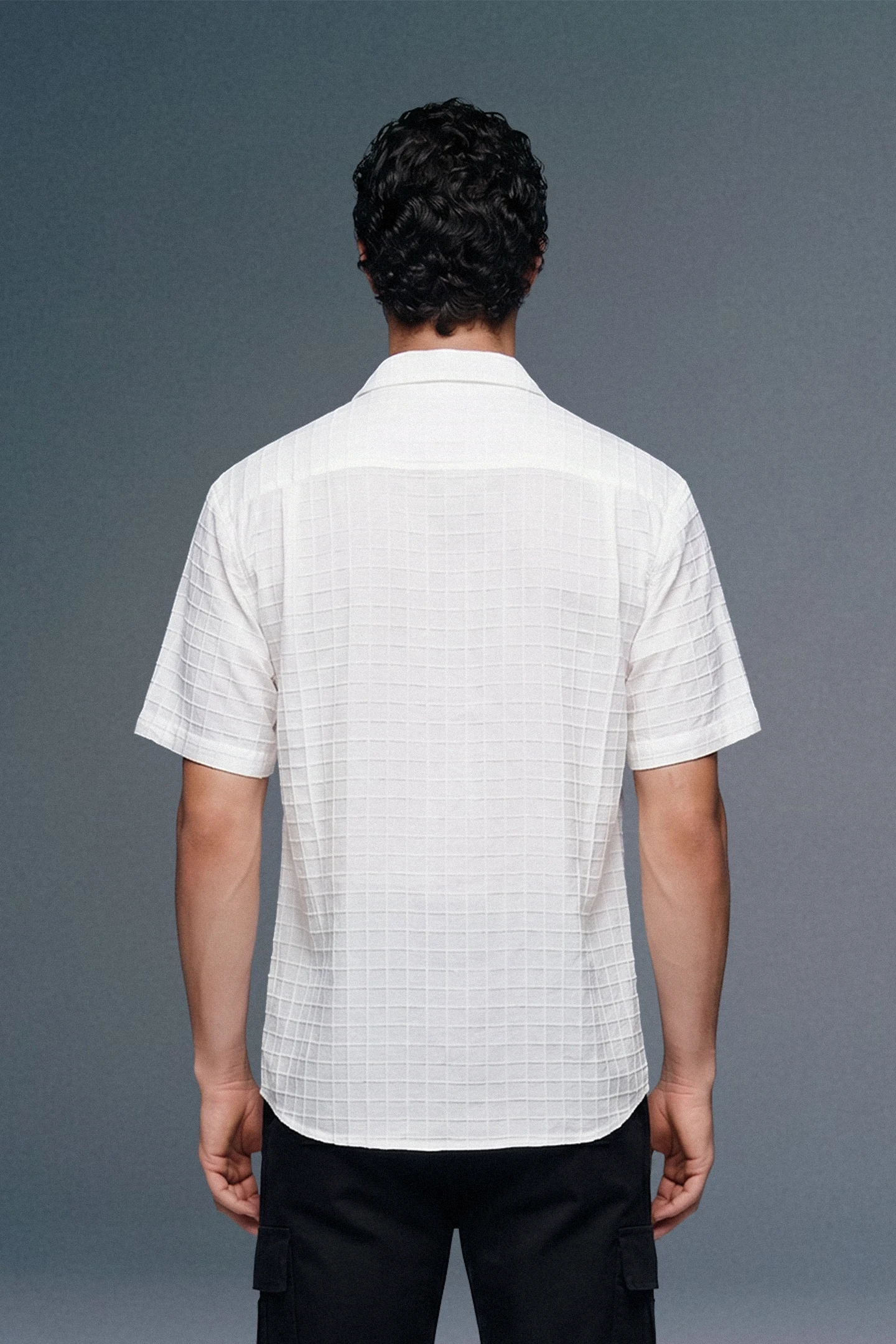 Man wearing a white short-sleeve shirt against a gray background