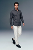 Man wearing a dark gray shirt and white pants on a plain background