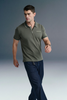 Full-length front view of a man walking forward at an angle, wearing an olive green polo shirt and dark blue jeans against a grey gradient background.