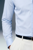 Light blue dress shirt with rolled-up sleeves and beige pants on a gray background