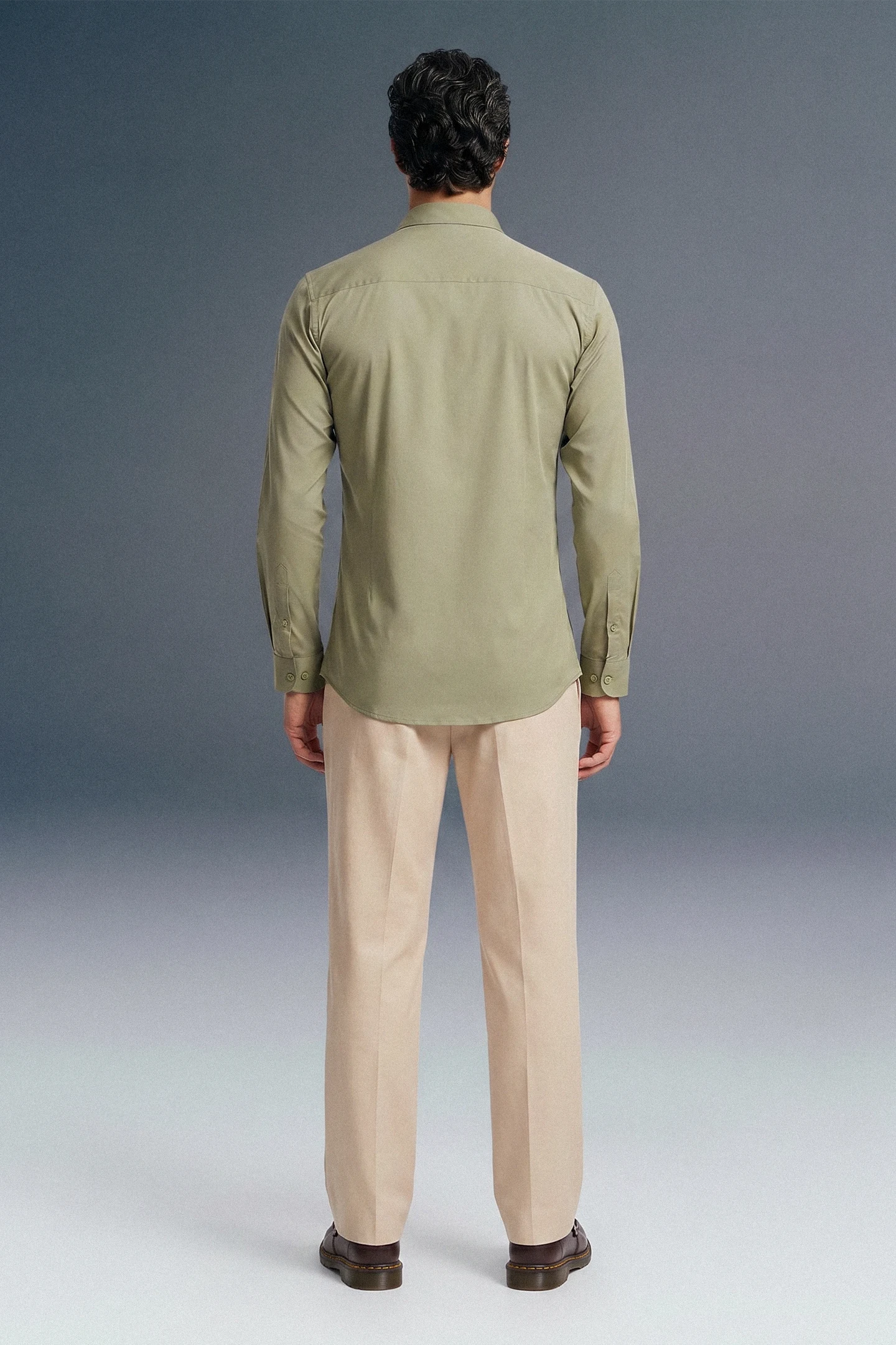 Person wearing a green shirt and beige pants against a gray background