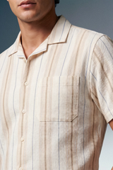 Close-up of a man wearing a beige striped shirt against a gray background