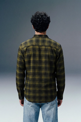 Person wearing a green and black plaid shirt with blue jeans against a gray background