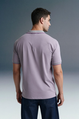 Rear view from the waist up of a man looking over his right shoulder, showcasing the back profile of a light purple polo shirt paired with dark trousers.