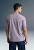 Rear view from the waist up of a man looking over his right shoulder, showcasing the back profile of a light purple polo shirt paired with dark trousers.