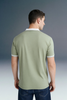 Rear view from the waist up of a man looking to the side, showcasing the back design of an olive green polo shirt with a white collar and white sleeve cuffs.