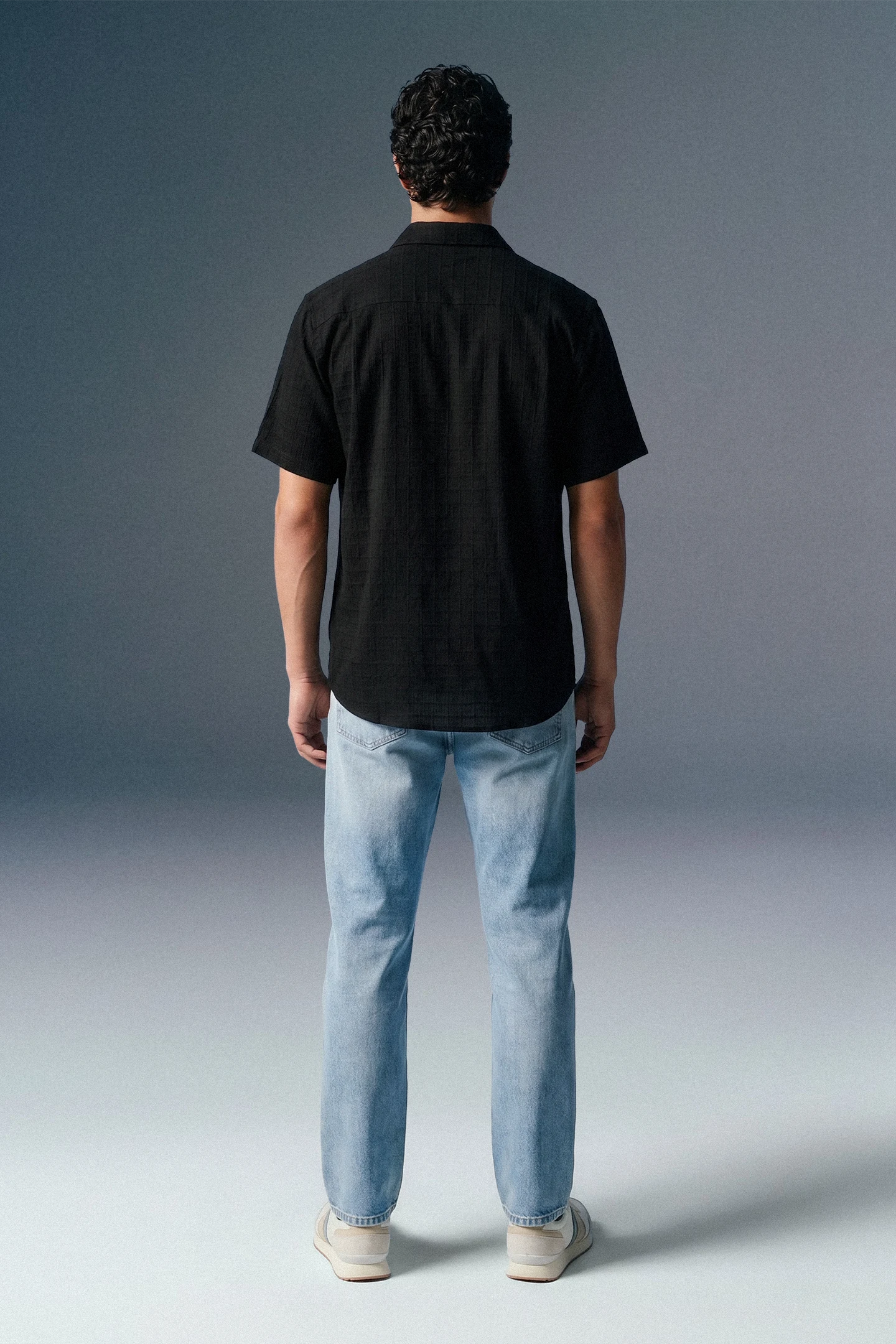 Person wearing a black shirt and light blue jeans against a gray background