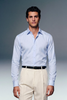 Man wearing a light blue dress shirt and beige pants against a gray background