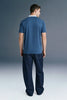 Full-length rear view of a man looking slightly down and to the right, wearing a slate blue polo shirt and dark trousers.