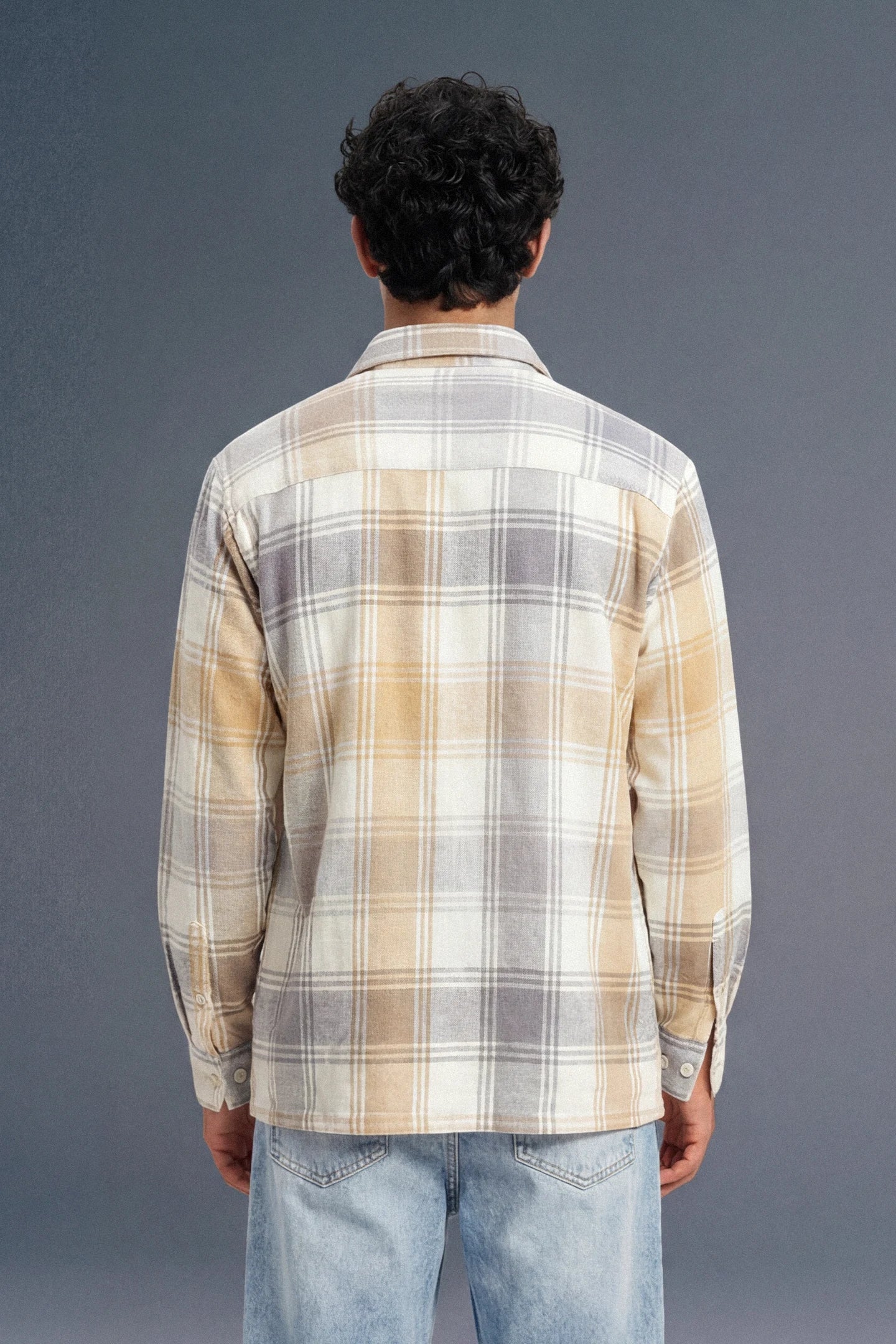 Person wearing a plaid shirt and jeans from behind on a gray background