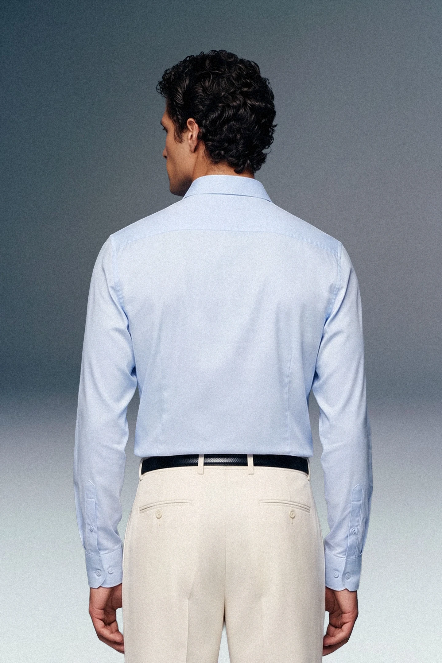 Man wearing a light blue dress shirt and beige pants against a gray background