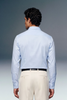 Man wearing a light blue dress shirt and beige pants against a gray background