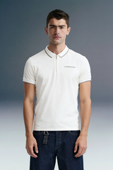 Three-quarter front shot from the waist up of a man facing forward, wearing a white polo shirt featuring a striped collar edge and small left-chest text.