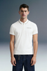Three-quarter front shot from the waist up of a man facing forward, wearing a white polo shirt featuring a striped collar edge and small left-chest text.