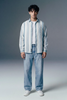 Person wearing a striped shirt and jeans against a gray background
