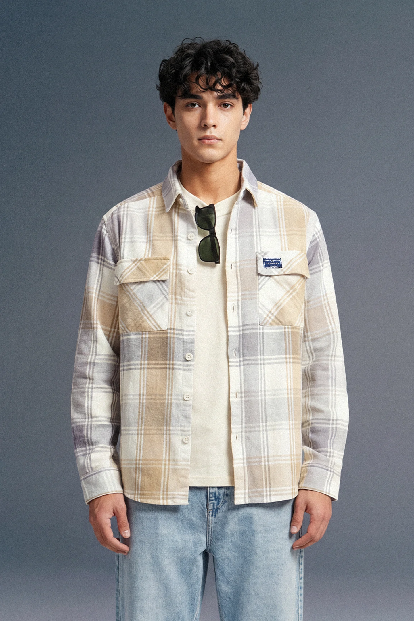 Man wearing a plaid shirt and jeans against a gray background