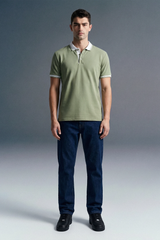 Full-length front view of a man standing straight and facing forward, wearing an olive green polo shirt with white trim and dark navy blue trousers.