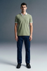 Full-length front view of a man standing straight and facing forward, wearing an olive green polo shirt with white trim and dark navy blue trousers.