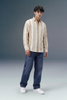 Man wearing a striped shirt and jeans standing against a plain background
