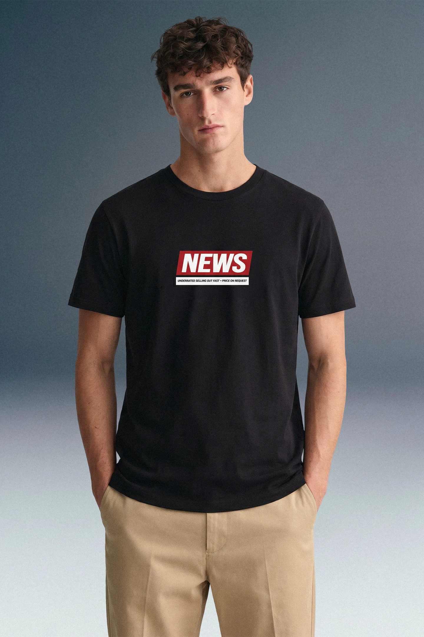 Front view from the waist up of a man looking directly forward with his hands in his pockets, highlighting the center-chest red graphic on his black crewneck T-shirt.