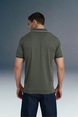 Rear view from the waist up of a man looking down and to his left, showing the back design and shoulder fit of an olive green polo shirt.