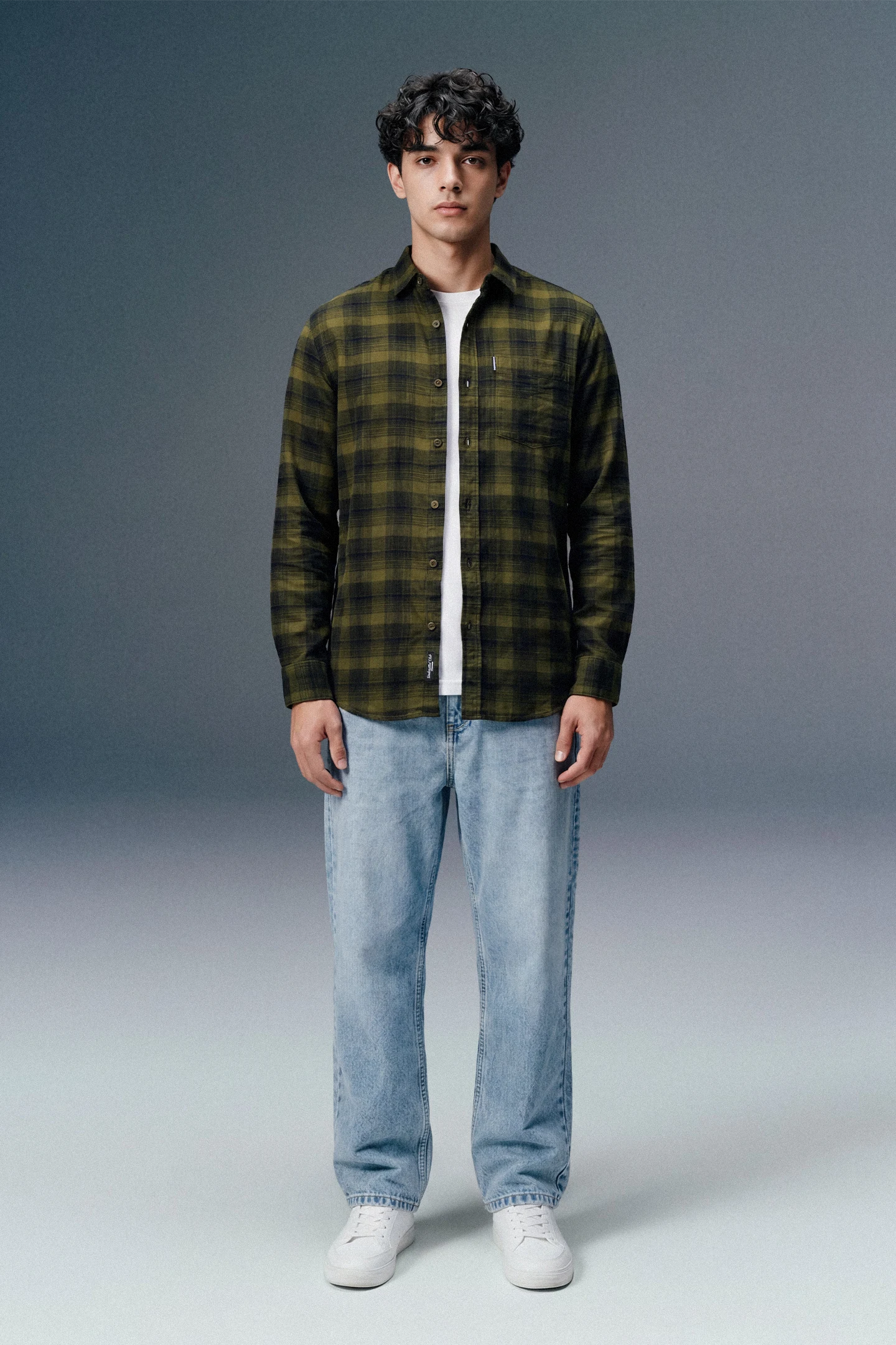 Person wearing a green plaid shirt, white t-shirt, light blue jeans, and white sneakers on a gray background