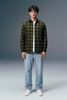 Person wearing a green plaid shirt, white t-shirt, light blue jeans, and white sneakers on a gray background
