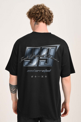 Back view of a man with curly hair wearing an oversized black t-shirt with a metallic-look graphic that reads 