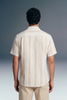 Man wearing a beige striped shirt and pants against a gray background