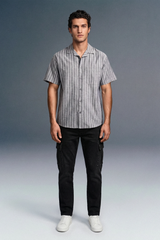Man wearing a striped shirt and black pants against a gray background
