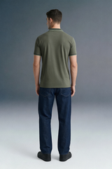 Full-length rear view of a man standing straight, wearing an olive green polo shirt featuring a thin light stripe on the collar, paired with dark navy blue trousers.