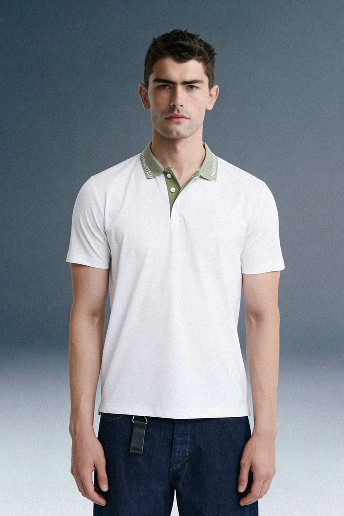 Full-length front view of a man standing facing forward, wearing a white polo shirt featuring a contrasting olive green collar, paired with dark blue trousers.