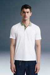 Full-length front view of a man standing facing forward, wearing a white polo shirt featuring a contrasting olive green collar, paired with dark blue trousers.