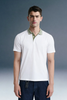 Full-length front view of a man standing facing forward, wearing a white polo shirt featuring a contrasting olive green collar, paired with dark blue trousers.