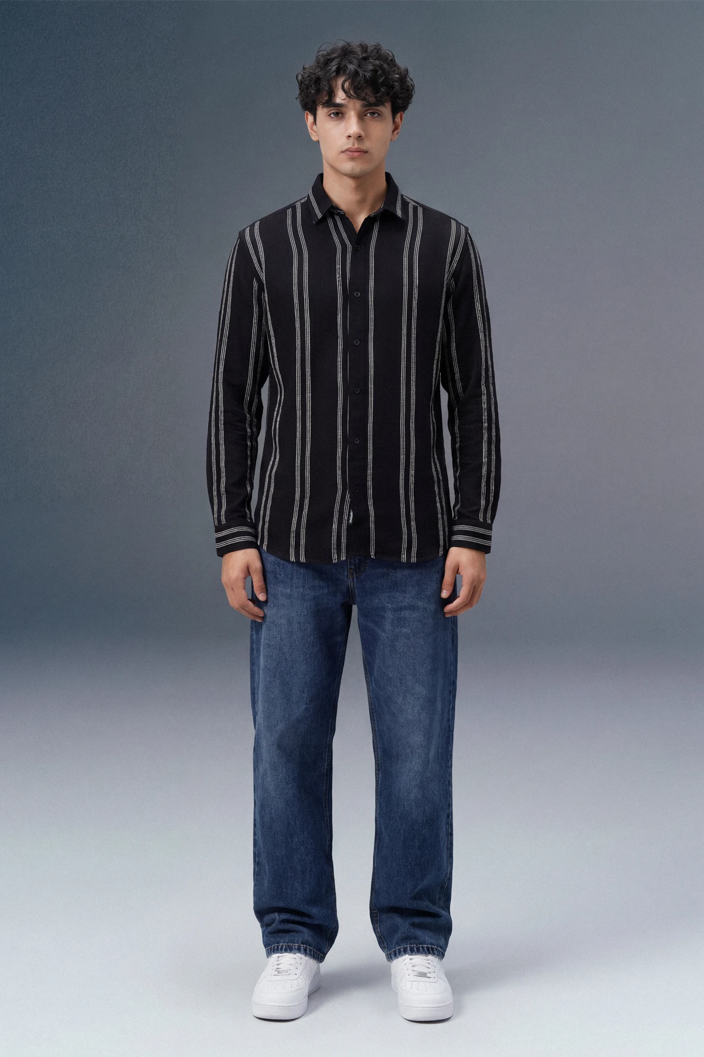 Person wearing a black striped shirt and blue jeans on a gray background