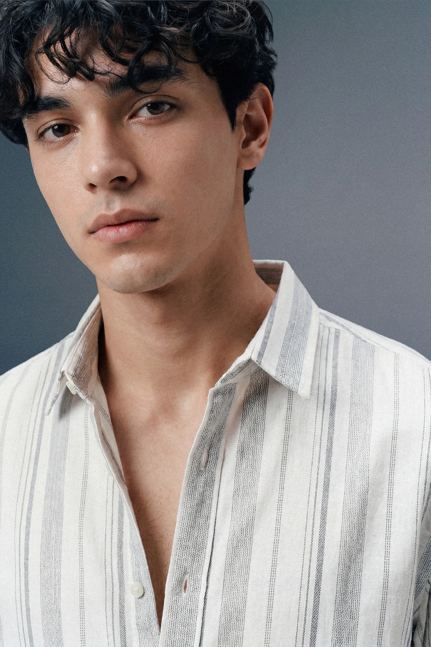Man wearing a light-colored striped shirt against a gray background