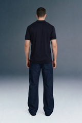 Full-length front view of a man mid-stride looking to his right, wearing a navy blue open-placket polo shirt and dark navy trousers.