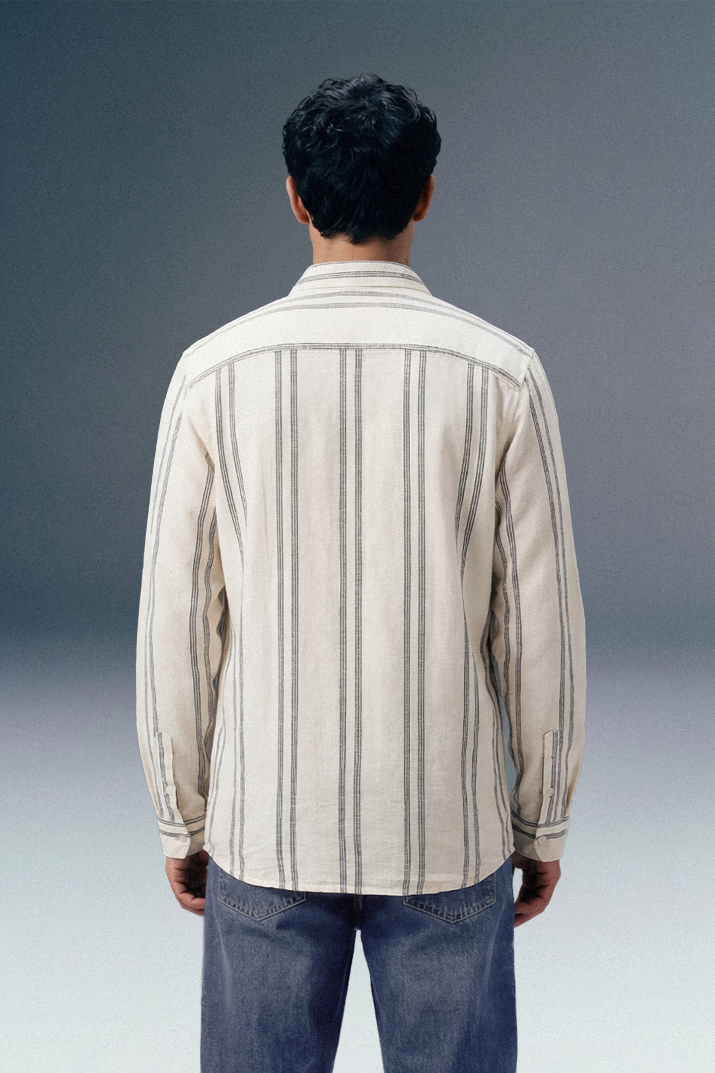 Man wearing a striped shirt and jeans from behind on a gradient background