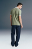 Full-length rear view of a man looking over his shoulder, wearing an olive green polo shirt with a white collar paired with dark navy blue trousers.