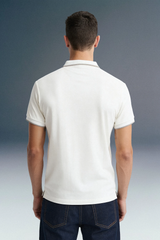 Rear view from the waist up of a man showing the back structure and clean collar line of a white polo shirt, worn with dark jeans.
