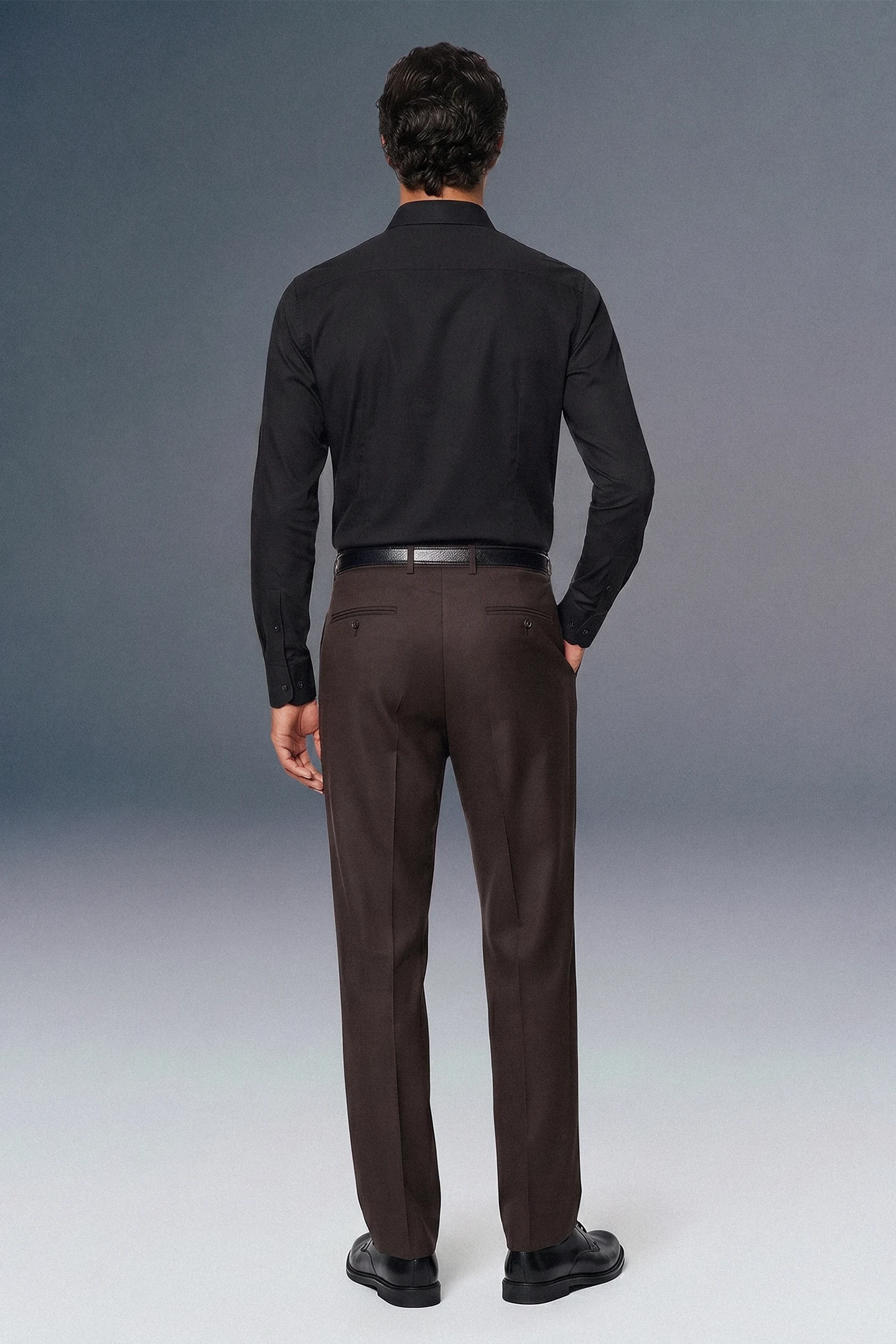 Man wearing a black shirt and brown pants against a gray background