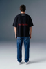 Full-length rear view of a man standing still, showcasing the complete back profile of a black graphic T-shirt paired with blue jeans.