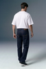 Person wearing a white t-shirt and dark jeans against a gray background
