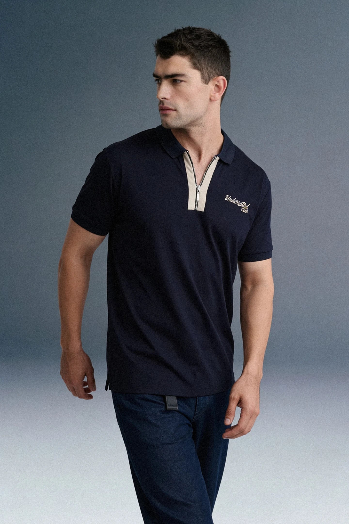 A dynamic, close-up angled shot from the chest up focusing on the arm and torso of a man leaning forward in a navy blue polo shirt with beige collar detailing.