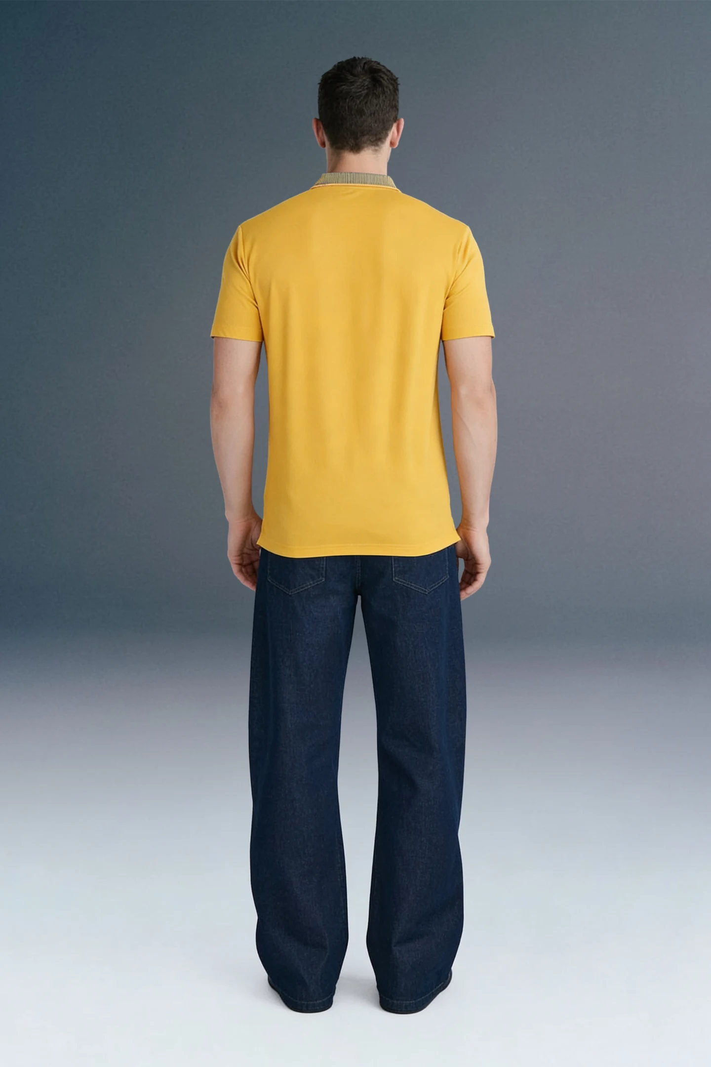 Full-length rear view of a man standing straight, wearing a mustard yellow polo shirt and dark navy blue trousers.