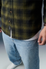 Person wearing a green plaid shirt, white t-shirt, blue jeans, and white sneakers on a light gray background